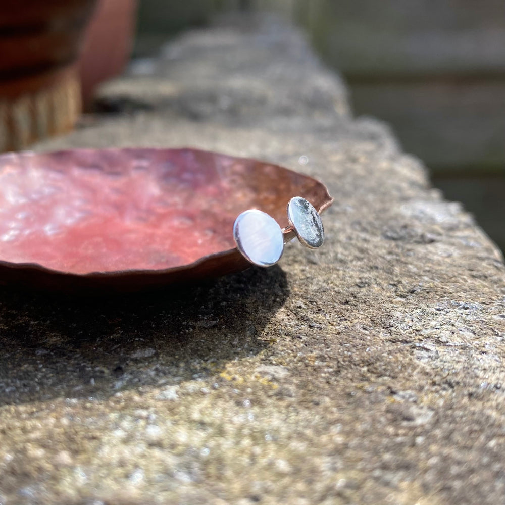 A pair of small smooth silver disk stud earrings, resting on the edge of a copper dish, by zoe ruth designs.