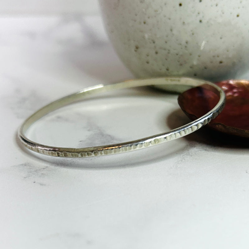 a thin width sterling silver bangle with a linear hammered texture