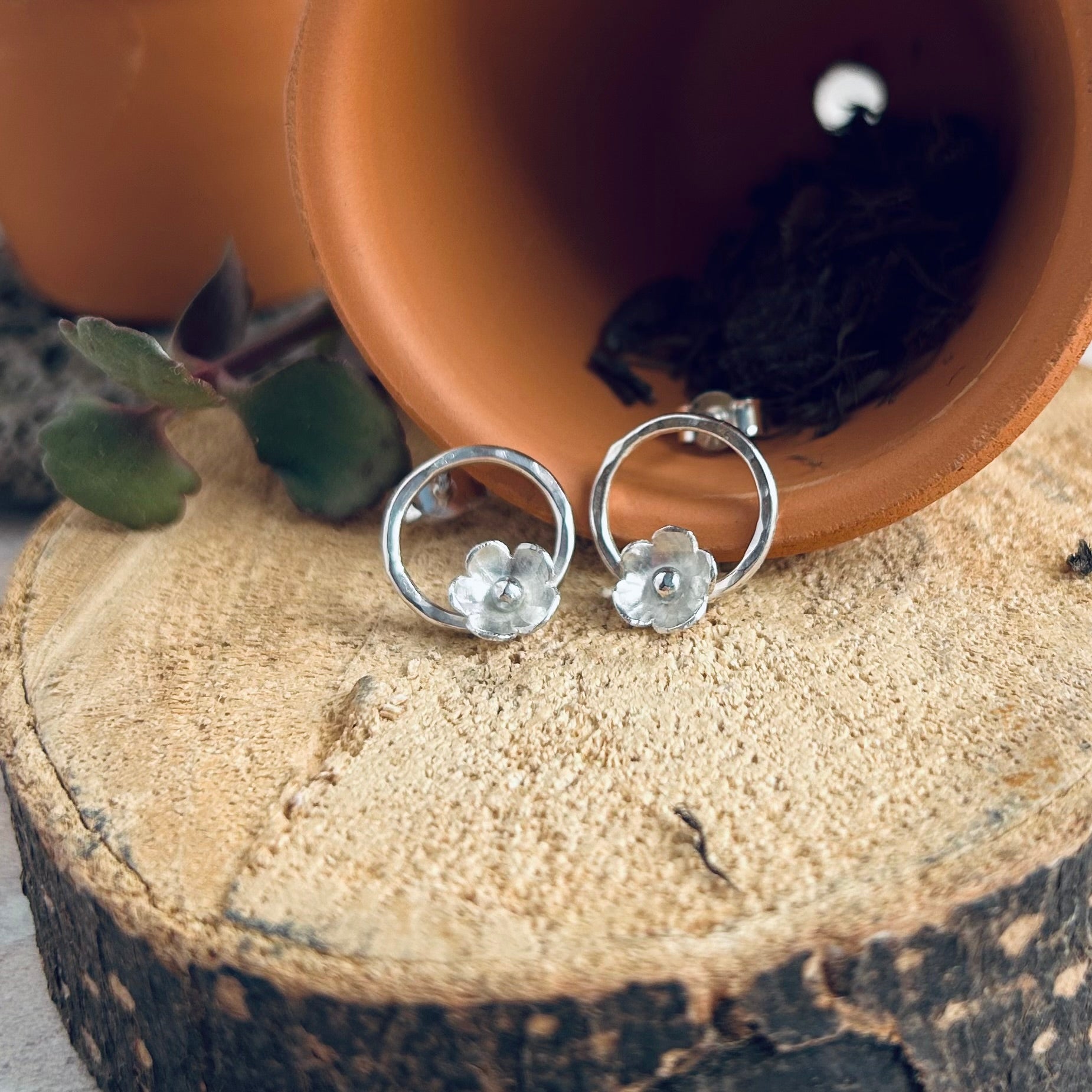 Two stud earrings, each with one sterling silver 5 petal flowers, hammered on the petals and with 3D silver ball centres, attached to the bottom of a small open circle, stud attached at the top, by zoe ruth designs