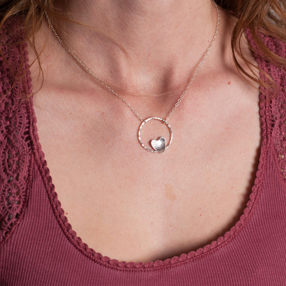 A silver heart and circle necklace on a person to show how it would look being worn.