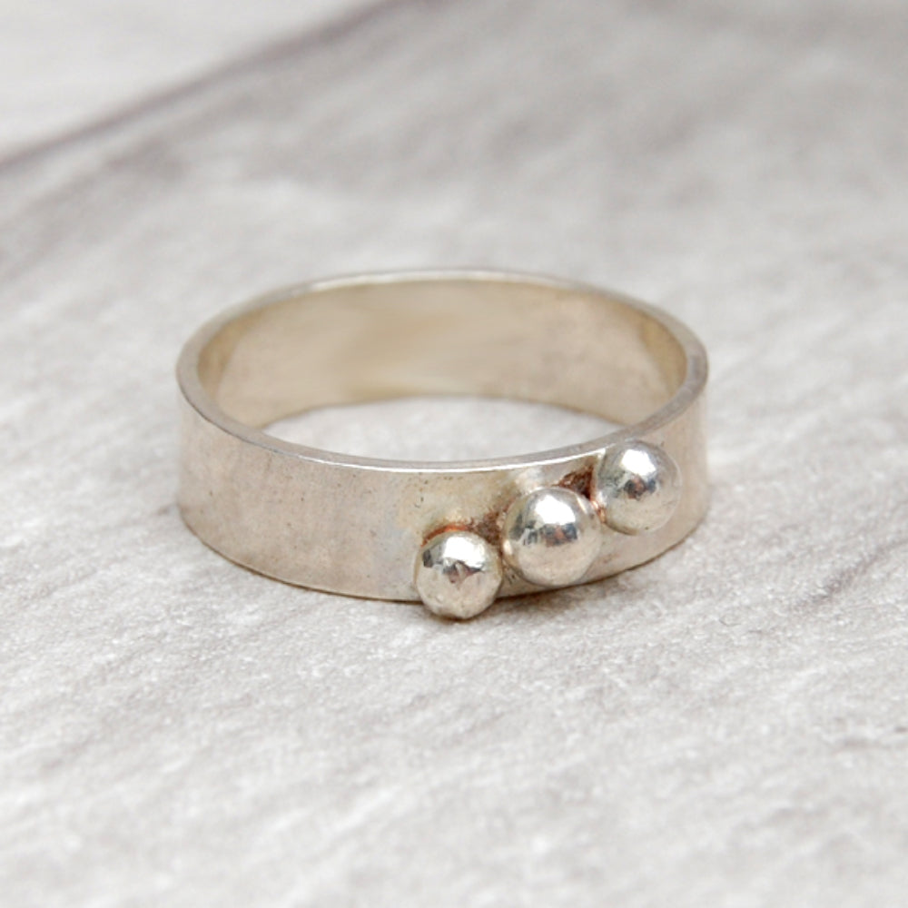 A 5mm wide smooth silver band with three silver balls soldered in a diagonalline across the width, b zoe ruth designs.
