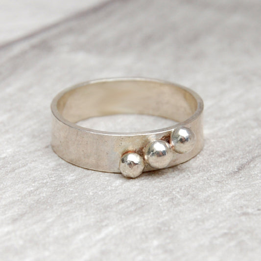 A 5mm wide smooth silver band with three silver balls soldered in a diagonalline across the width, b  zoe ruth designs.