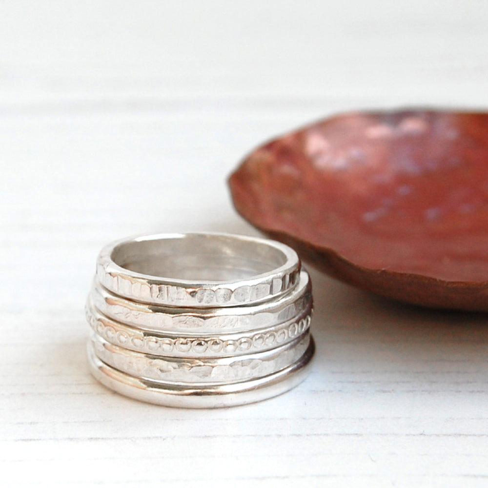 Showing five silver stacking rings with different surface textures, by zoe ruth designs