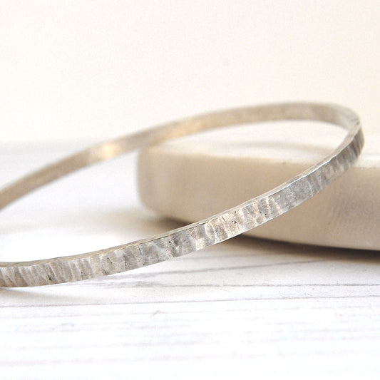 Showing a silver bangle with a linear tree bark like texture, by zoe ruth designs