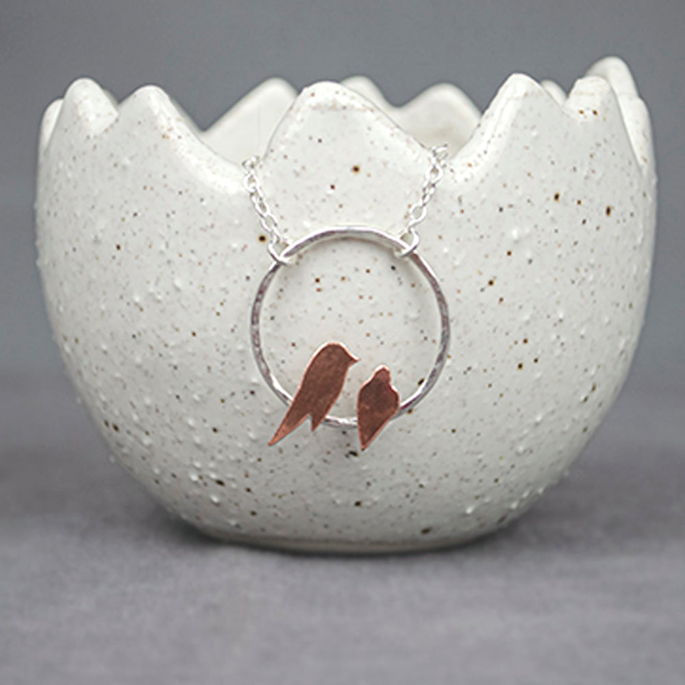 Two small hand sawn copper birds roosting on a hammered silver circle necklace by Zoe Ruth Designs