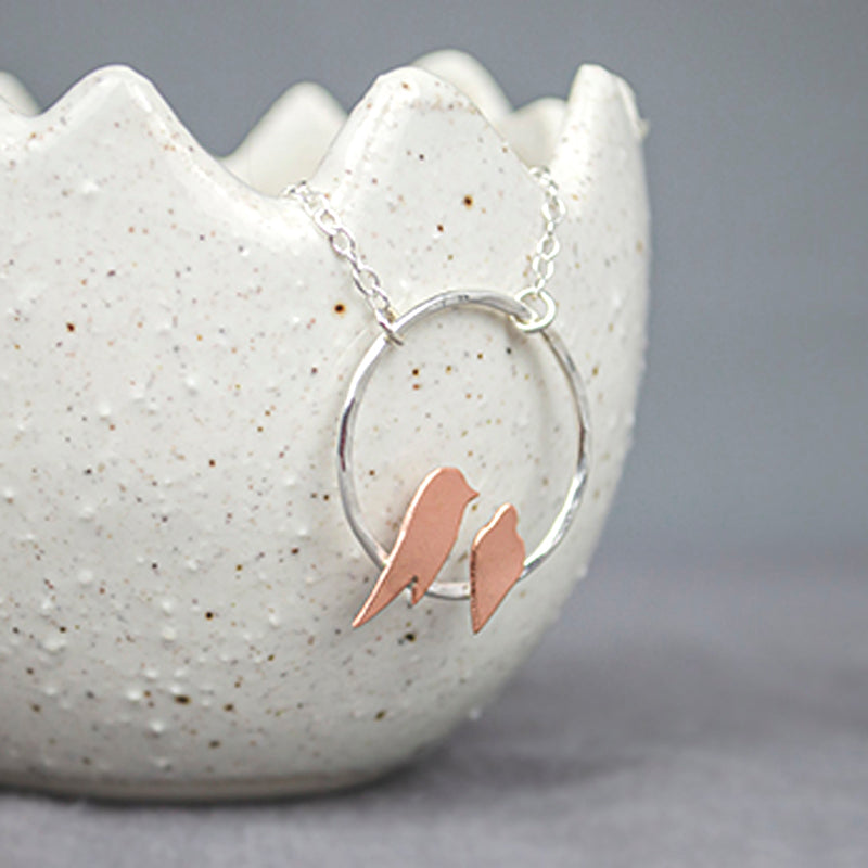 Two small hand sawn copper birds roosting on a hammered silver circle necklace by Zoe Ruth Designs