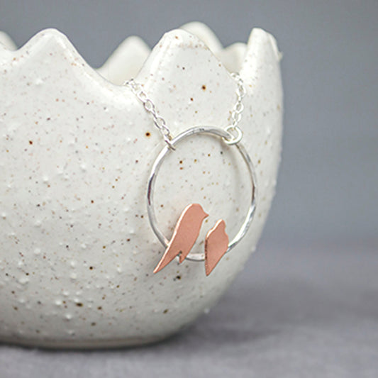 Two small hand sawn copper birds roosting on a hammered silver circle necklace by Zoe Ruth Designs