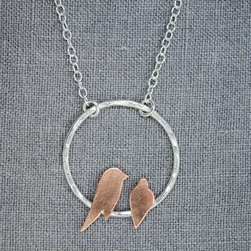 Two small hand sawn copper birds roosting on a hammered silver circle necklace by Zoe Ruth Designs