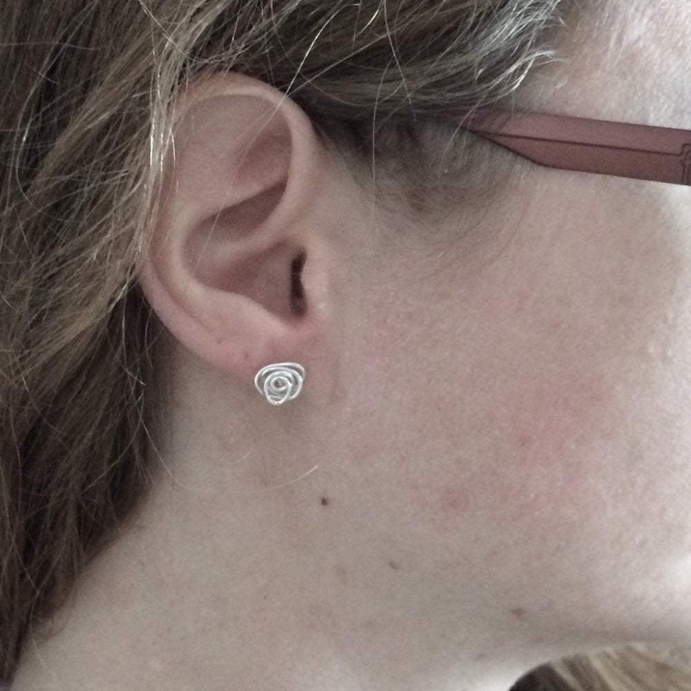 A pair of silver stud earrings each made from a messy coil of sterling silver wire, being worn, by zoe ruth designs.