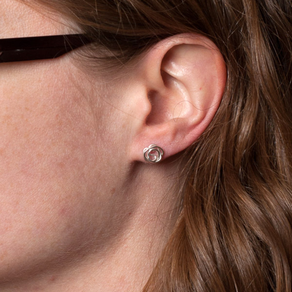 A pair of silver stud earrings each made from a messy coil of sterling silver wire, being worn by zoe ruth designs.