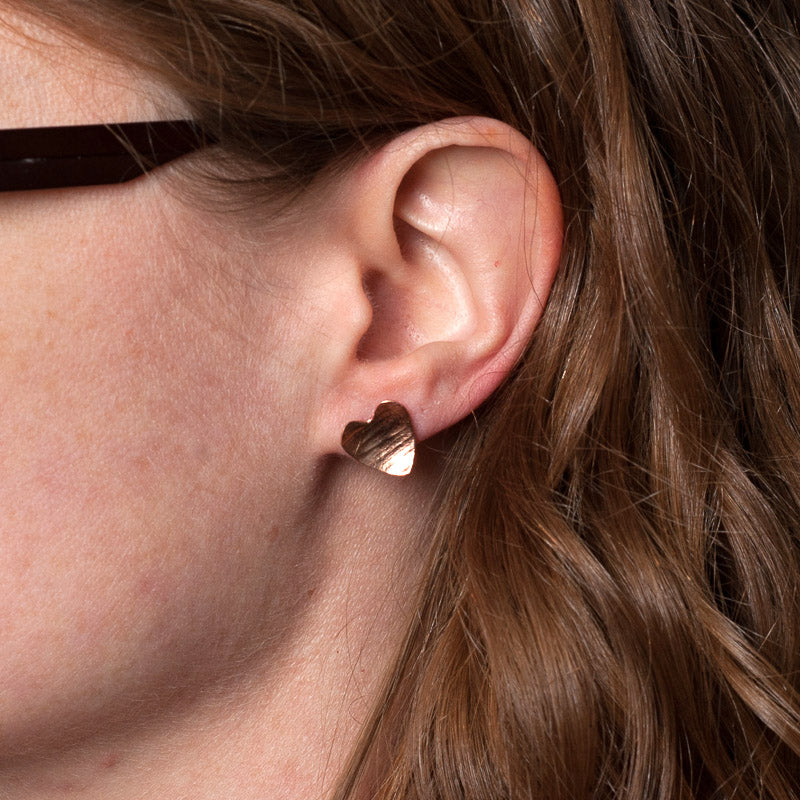 Heart shaped hammered with a lines texture copper stud earrings, being worn by zoe ruth designs