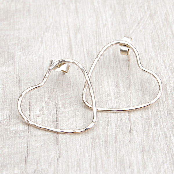 Two silver heart stud earrings, made from hammered wire to give the outline of hearts, the earring stud placed on opposing sides, by zoe ruth designs