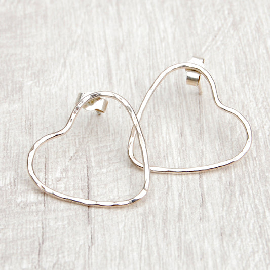 Two silver heart stud earrings, made from hammered wire to give the outline of hearts, the earring stud placed on opposing sides, by zoe ruth designs