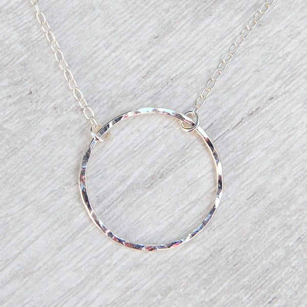 A slim circle frame pendant, sterling silver and lightly hammered, hangs from a sterling silver chain, shown catching the light, by zoe ruth designs.
