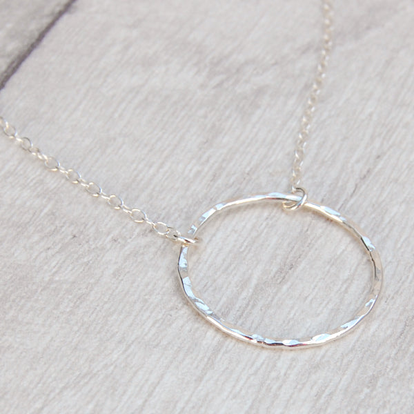 A slim circle frame pendant, sterling silver and lightly hammered, hangs from a sterling silver chain, shown catching the light, by zoe ruth designs.
