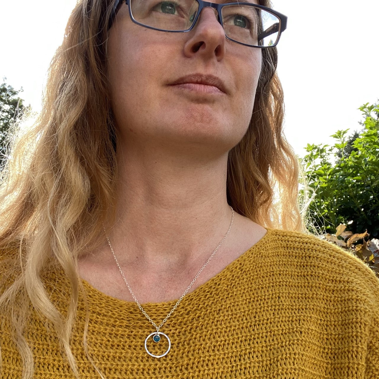 A 5mm semi preciouse stone set in silver hangs loosely at the top of a larger slim and hammered circle frame as the pendant of this necklace being worn by zoe ruth designs.
