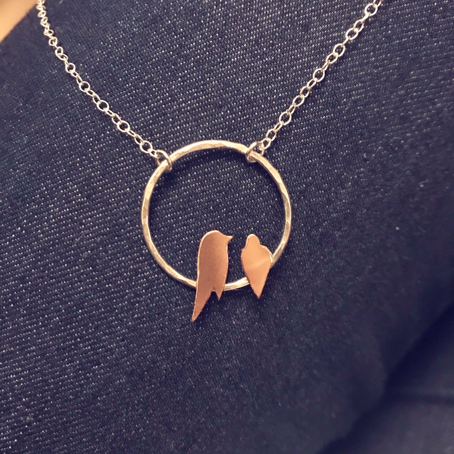 Two small hand sawn copper birds roosting on a hammered silver circle necklace by Zoe Ruth Designs