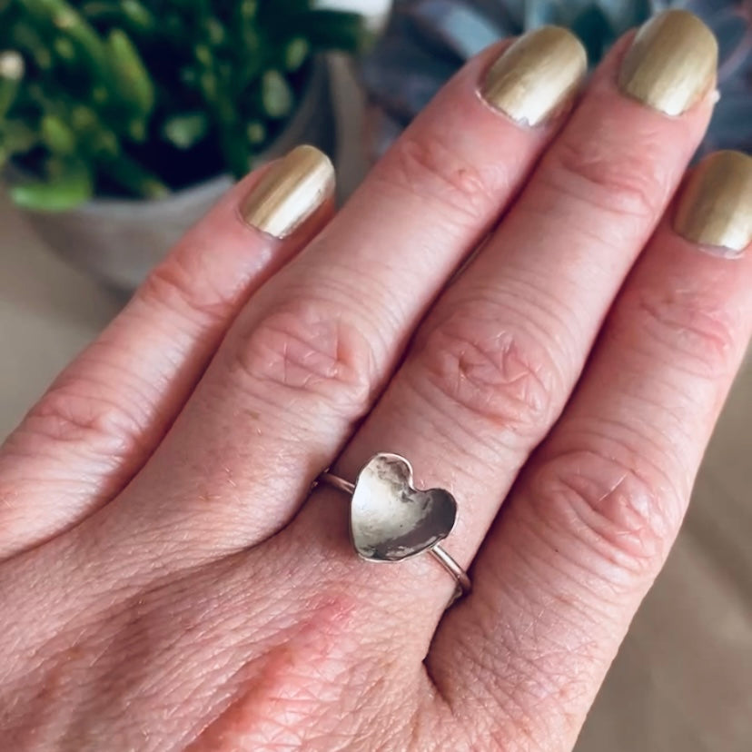 Hammered silver heart on a thin round silver wire ring being worn, by zoe ruth designs