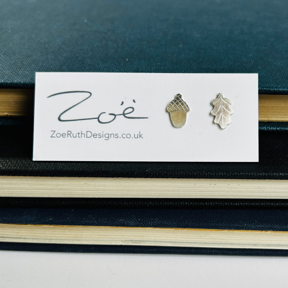 Handmade sterling silver stud earrings, an acorn and oak leaf, displayed on their logo card packaging of Zoe Ruth Designs