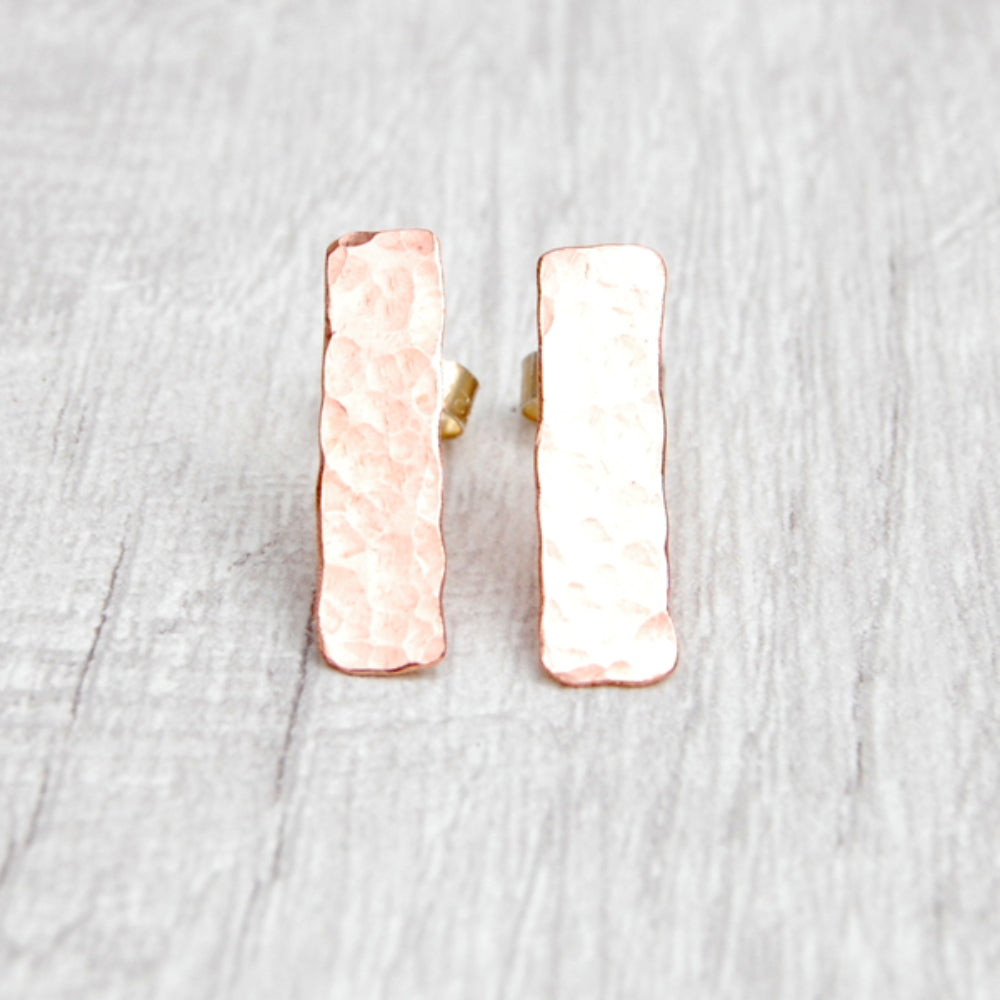 Slim rectangle shaped hammered surface copper stud earrings, diplayed to catch the light, by zoe ruth designs