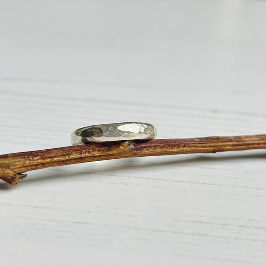 A classic dimple hammer texture on a D profile silver ring, sat tilted towards the light on a garden twig, by zoe ruth designs