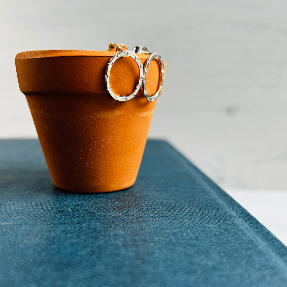 showing the shine on a pair of handmade silver stud earrings, oval in shape with a circle and dot stamped texture by zoe ruth designs