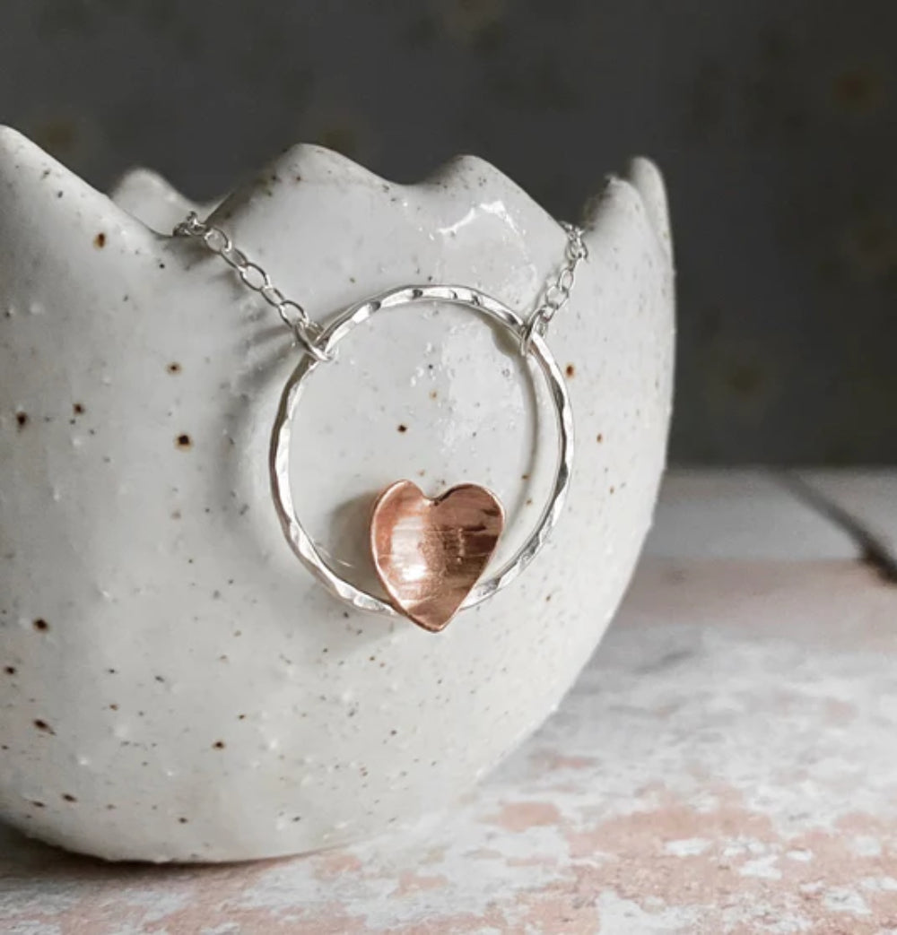 A hammered copper heart sits on the outline of a circle in sterling silver making a beautiful necklace design by zoe ruth designs