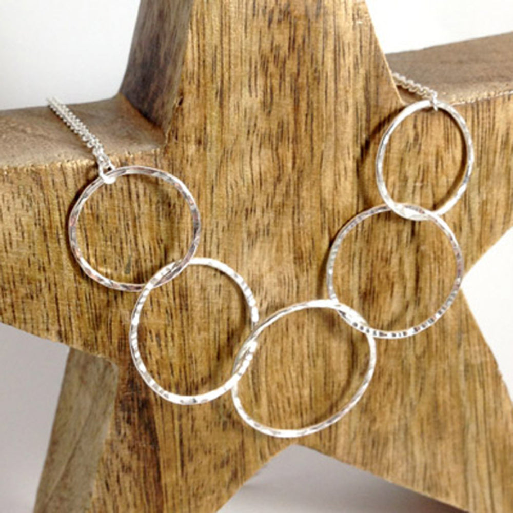 A handmade necklace made up of five open circle forms each linked through another, attached to a silver trace chain, by zoe ruth desigsns