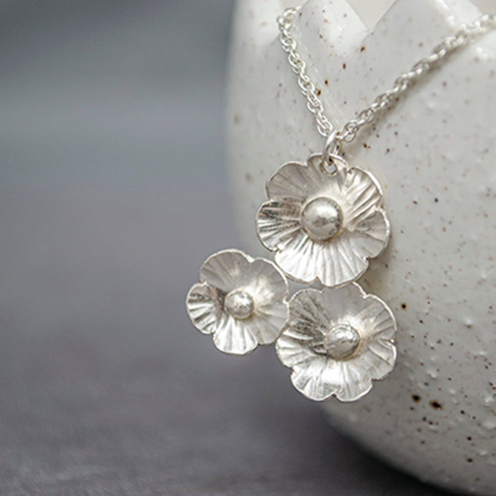 Three handmade silver flowers sit in a cluster and hand from a sterling silver chain, by zoe ruth designs