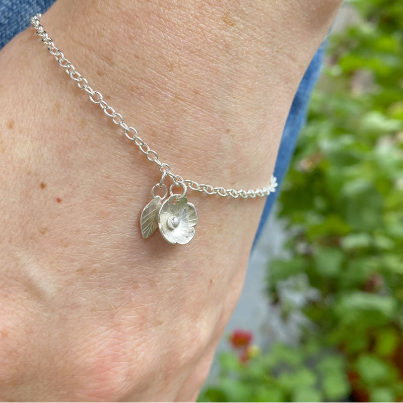 Silver flower and silver leaf hanging delicately from a silver bracelet chain on a persons wrist, by zoe ruth designs