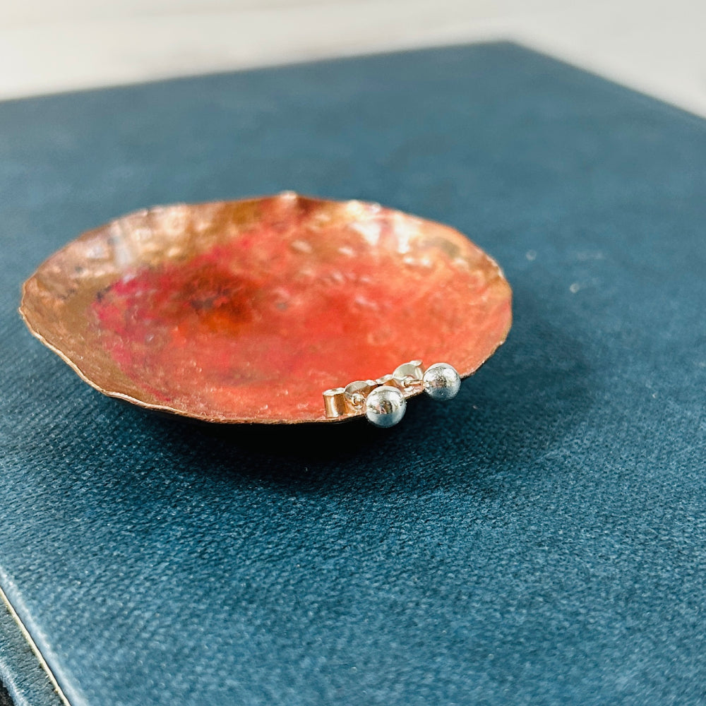 small silver ball studs resting on a copper dish, which is sat on a blue book, by zoe ruth designs