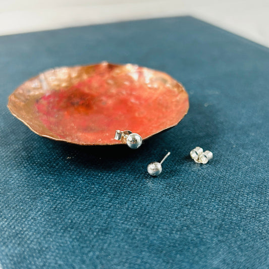 small silver ball studs, one resting on a copper dish, one on the blue book surface next to the dish, by zoe ruth designs