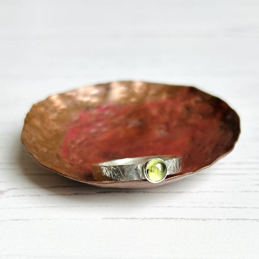 A pale green peridot stone bezel set on a textured sterling silver ring band