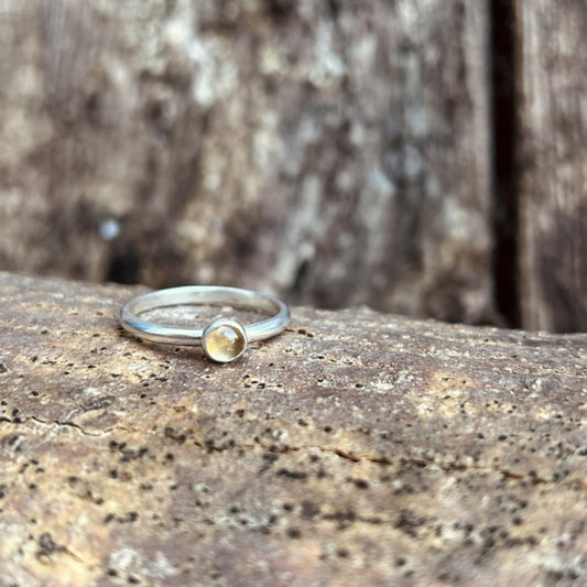 A yellow citrine cabochon stone set onto a silver ring sits ontop of a wooden surface.