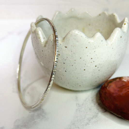 A slender sterling silver handmade bangle with a lines texture on the surface