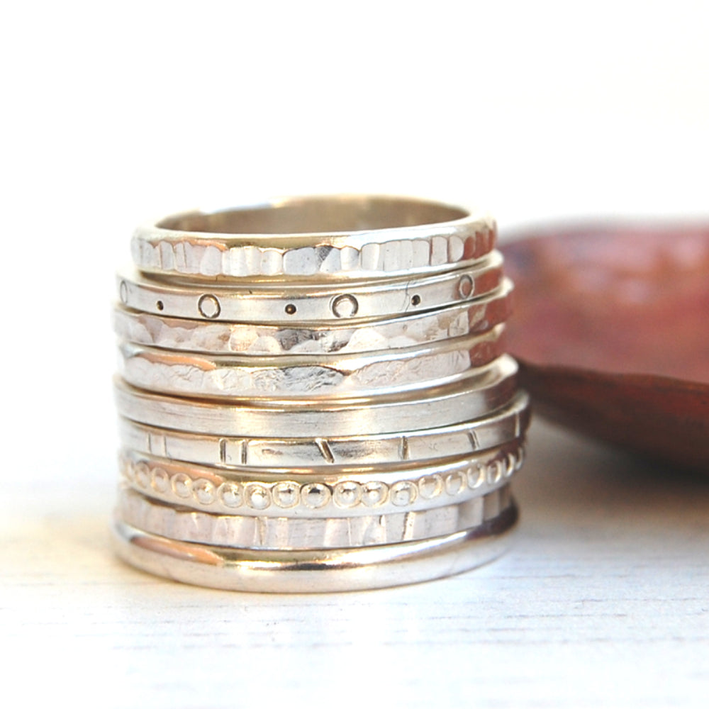 Showing nine silver stacking rings stacked up next to a copper dish all with different textures, by zoe ruth designs.