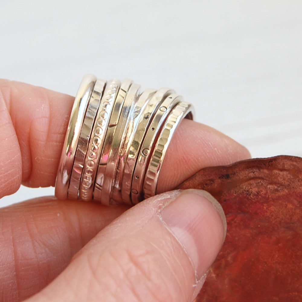 Showing nine silver stacking rings displayed on a finger, all with different textures, by zoe ruth designs.