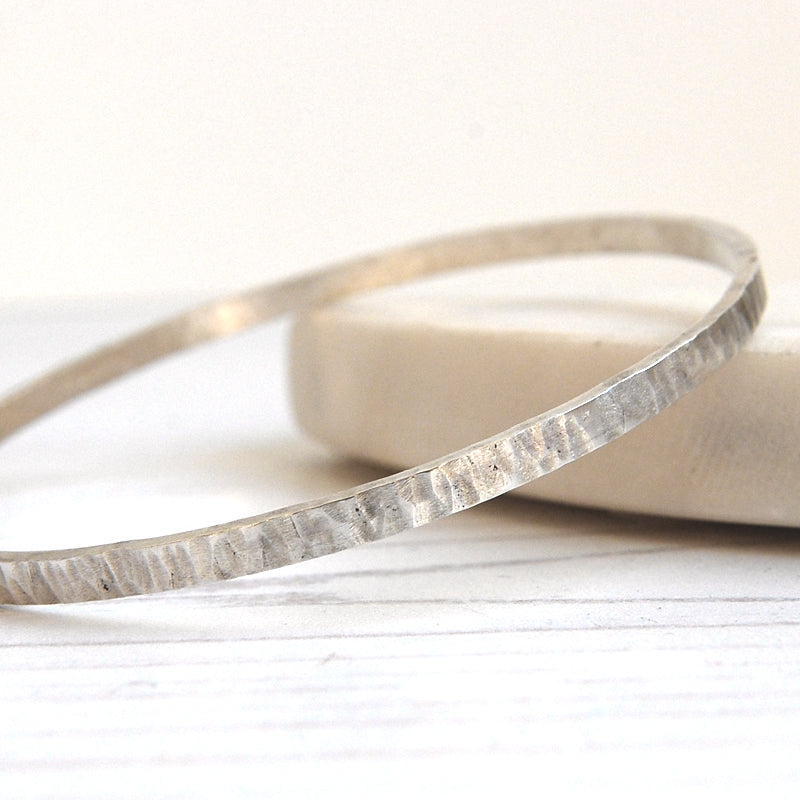 a close up of the hammered surface texture of a silver bangle, it is similare to the lines in tree bark