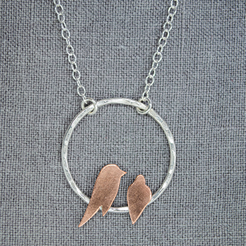 Two copper birds roosting on a sterling silver circle necklace on grey background by Zoe Ruth Designs