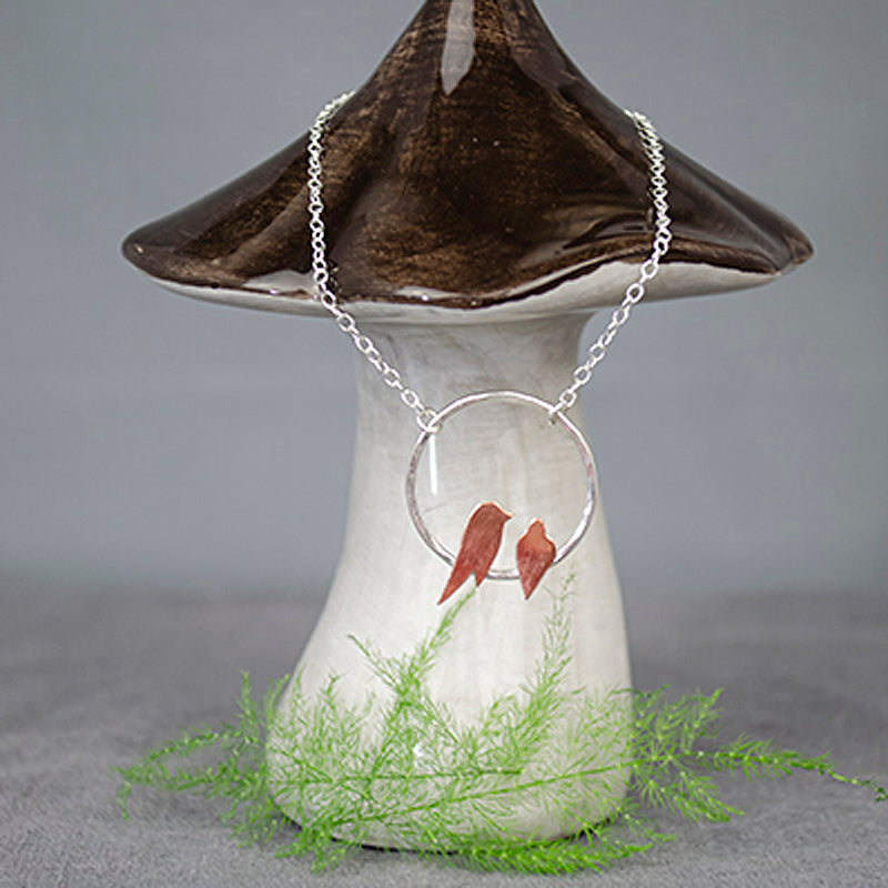 Necklace by Zoe Ruth Designs, two copper birds roosting on a silver circle, shown displayed on a ceramic mushroom