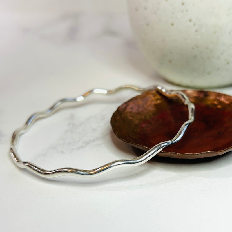 The sterling silver wire of this round, smooth and shiny bangle is wavy.