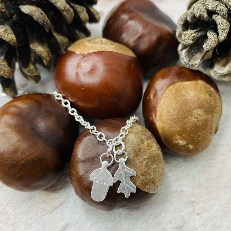 Handmade silver acorn and oakleaf bracelet displayed on conkers and pinecones