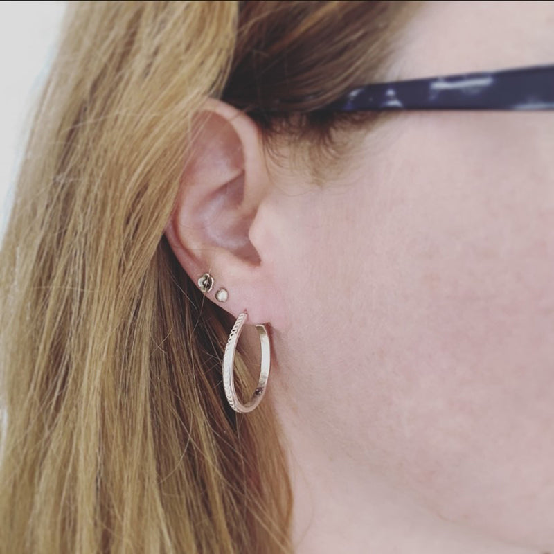 three earrings being worn in ear of female with glasses