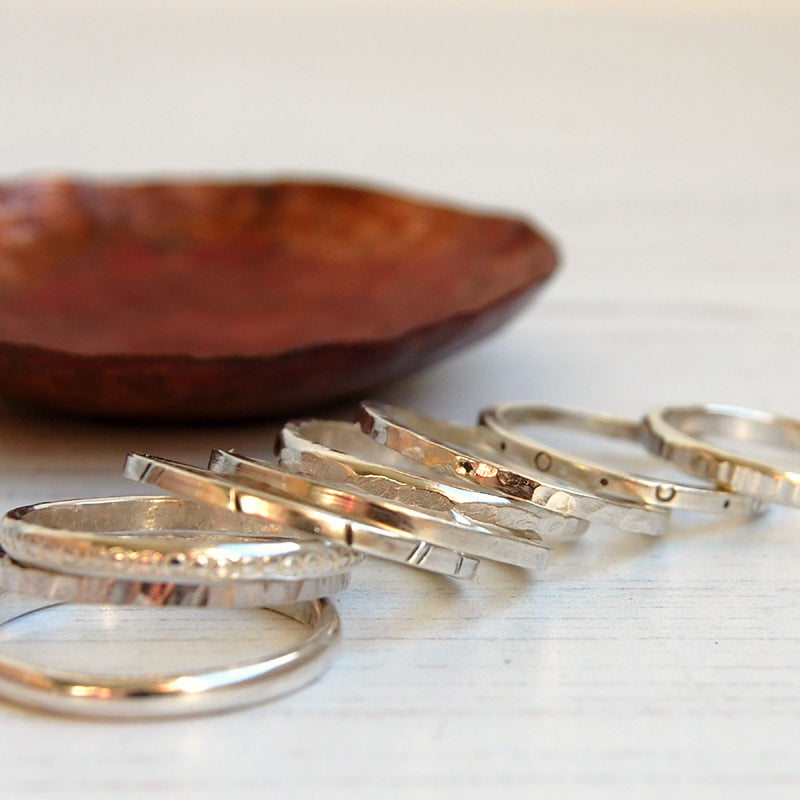 A scattered stack of handmade textures silver rings by zoe ruth designs